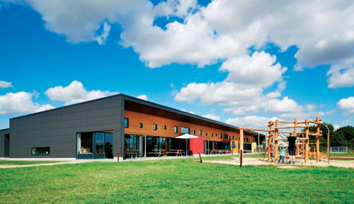 På billedet ser du en del af daginstitutionens bygning i Lund Børnehus og en legeplads med børn